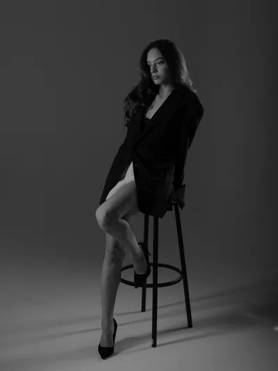 Full-length black-and-white portrait of Megann seated in a black blazer at a Tbilisi photo studio