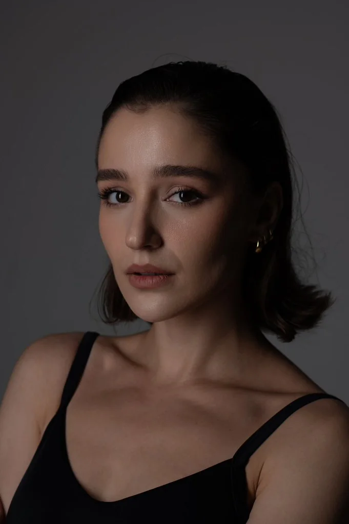 Professional studio headshot of Ninia in a black top against a gray background