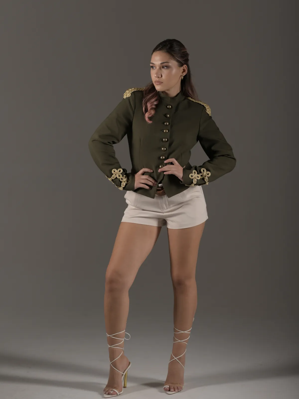 Model in an olive military-style jacket with gold embroidery posing for a fashion lookbook shoot in a Tbilisi studio