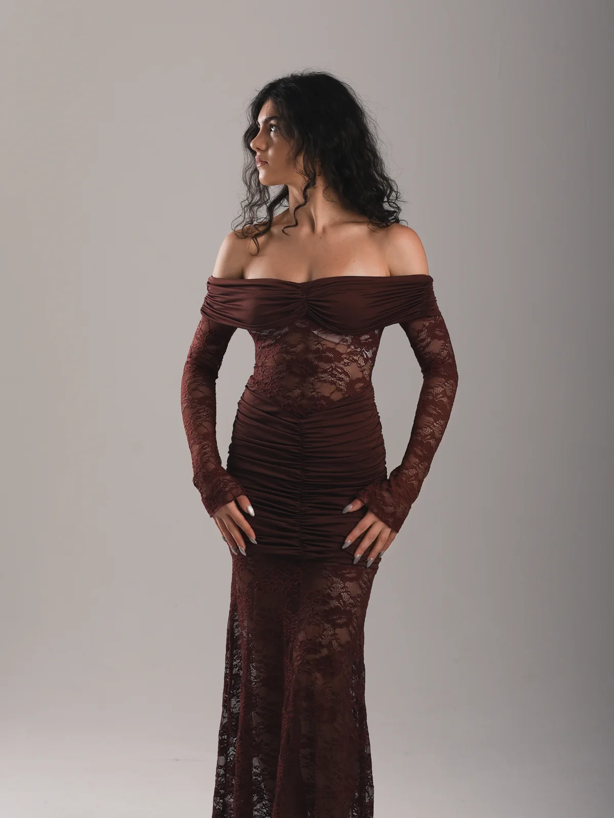 Mariami in profile modeling a burgundy lace evening dress in a photo studio