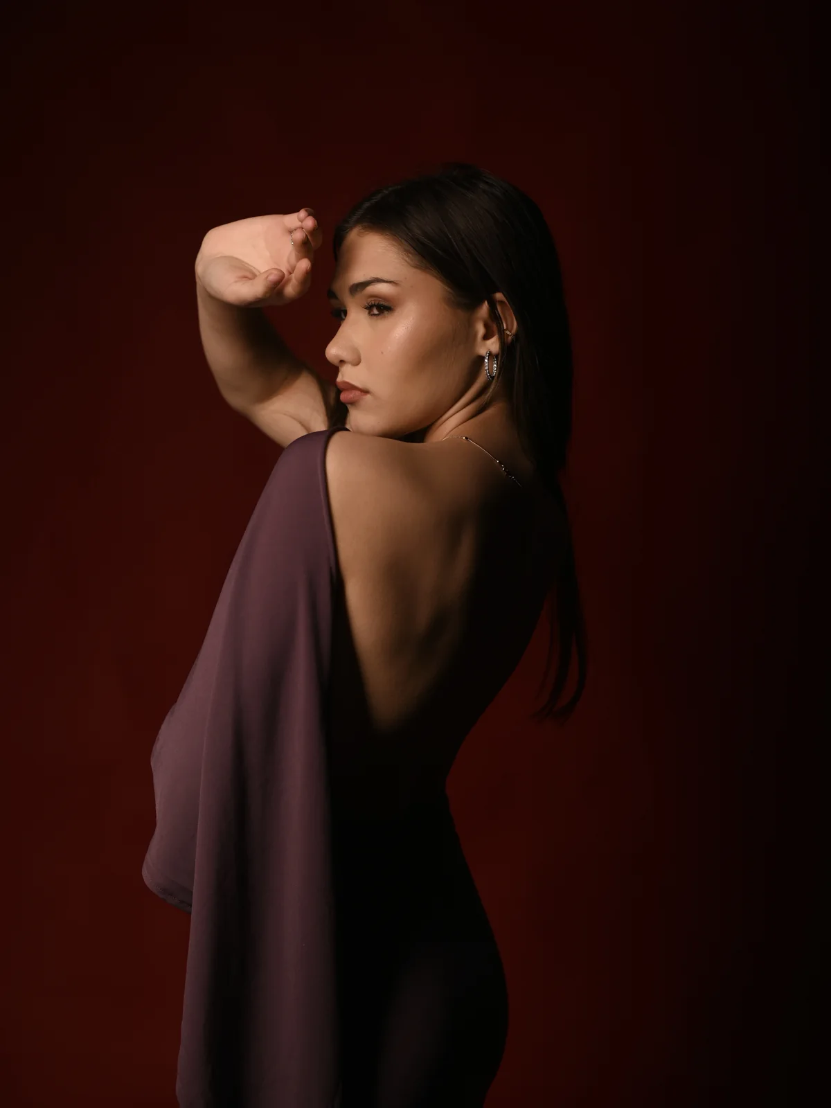 Mariam wearing a backless burgundy evening dress against a deep red studio background