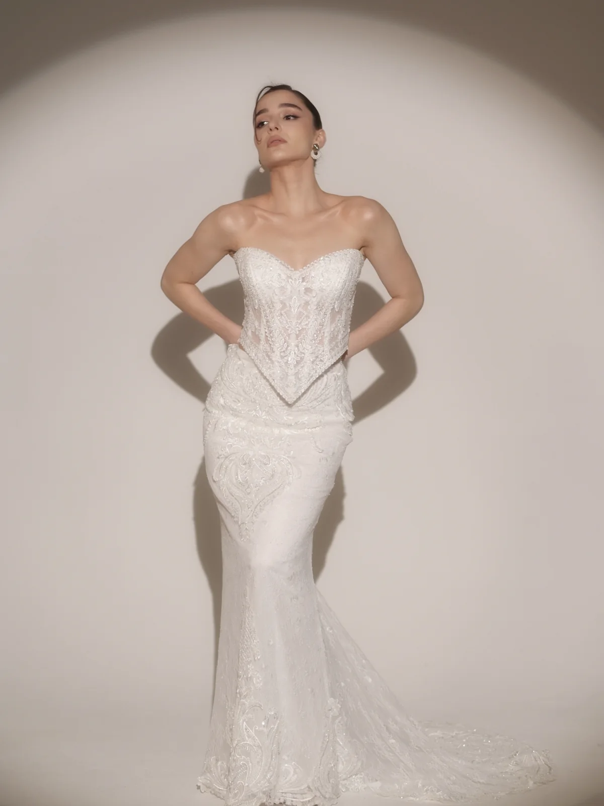 Ninia modeling a fitted white wedding dress under a dramatic studio spotlight