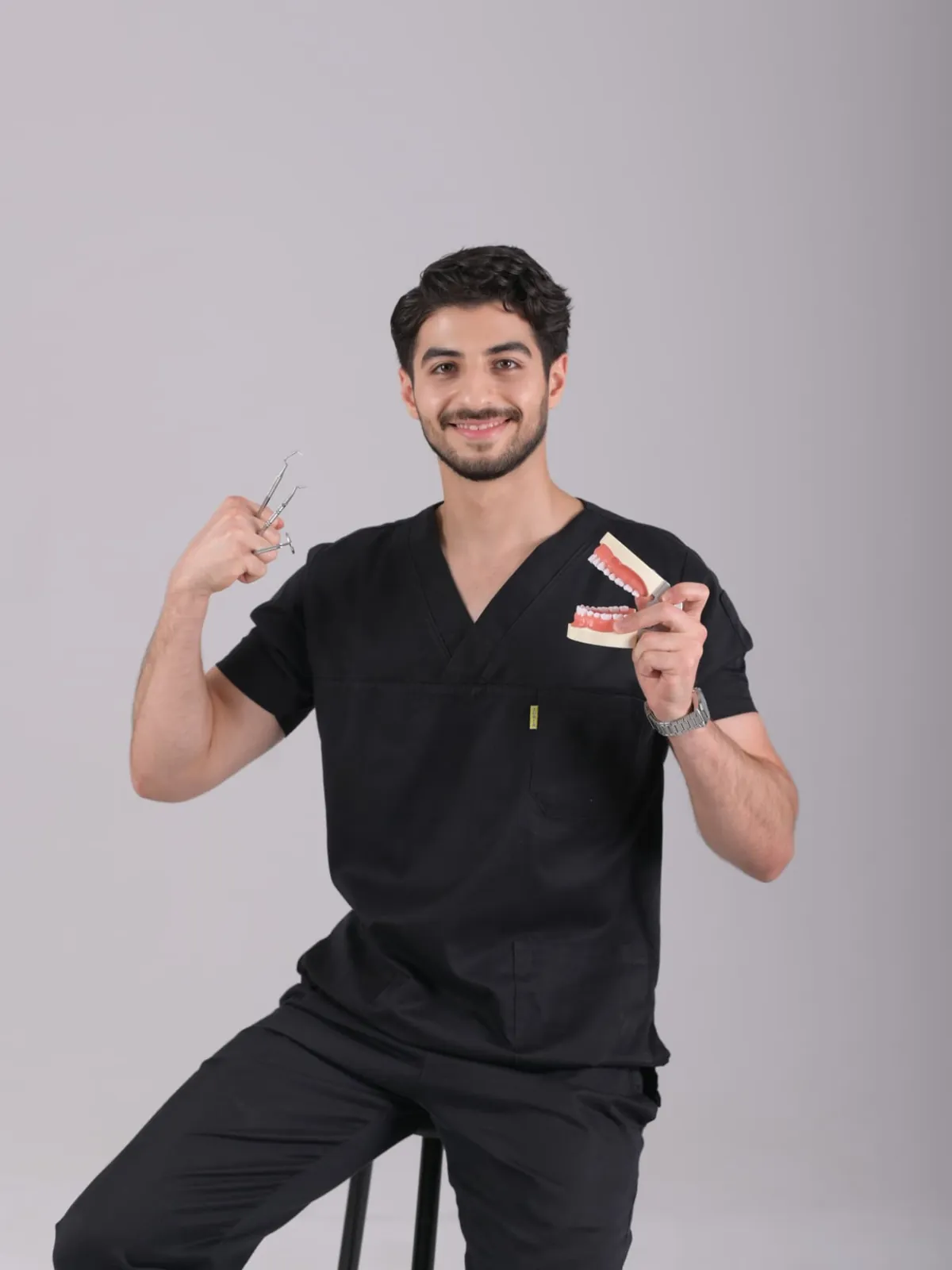 Medical student in black scrubs holding dental instruments and a jaw model during a graduation photo studio session in Tbilisi