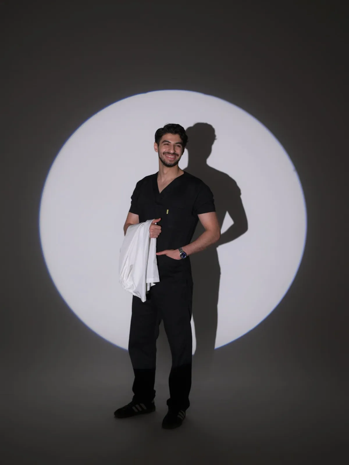 Full length graduation portrait of a medical student with a white coat, lit by a circular spotlight in a Tbilisi studio
