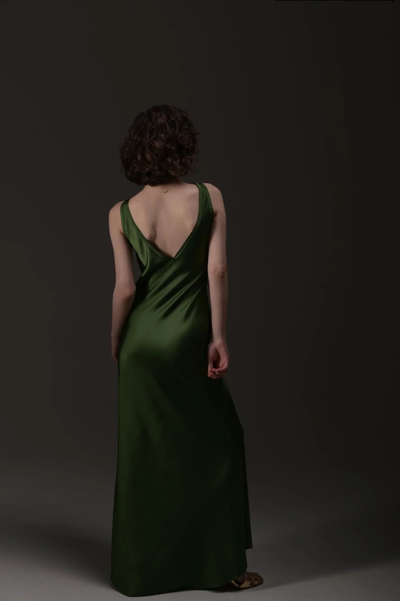 Back view of Lizi modeling an elegant green dress in a professional studio